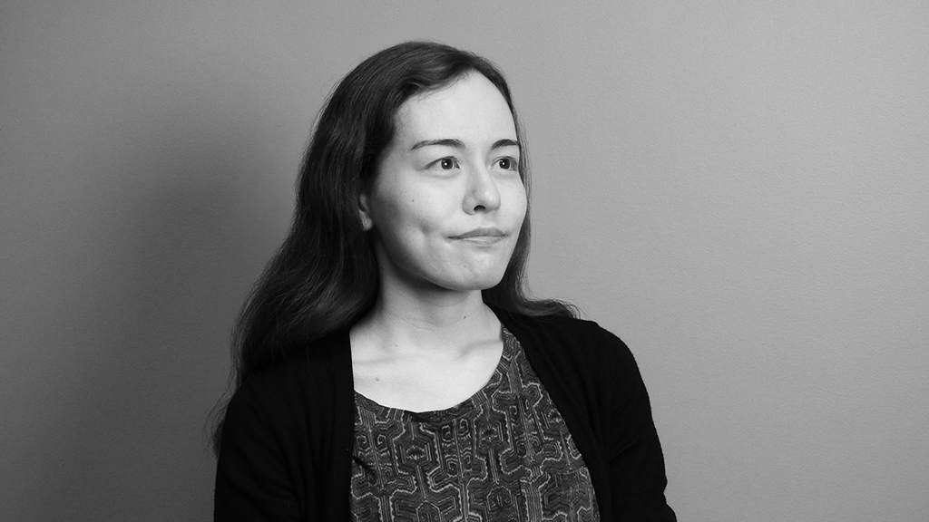 A black and white portrait of Alisa Brandt, a renowned medical illustrator with XVIVO, features her long hair gently flowing as she gazes slightly to the right. She wears a patterned top and a dark cardigan, set against a plain background, capturing an elegant blend of art and science.